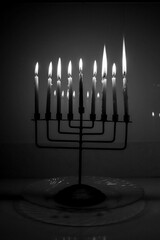 Black and white of a full menorah on the last night of Hanukkah. All nine candles are lit in a dark room and reflecting in the background