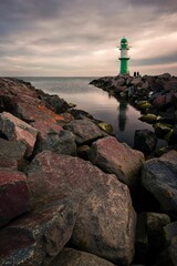 Vertical shot of a green lighthouse on the coast in cloudy sky background