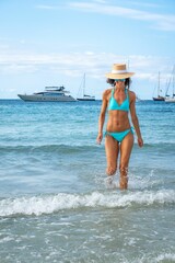 Fototapeta na wymiar Attractive Caucasian female in a bikini and a hat posing at the beach on a sunny day