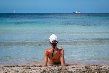 Attractive Caucasian female in a coral bikini and a cap sunbathing on the beach