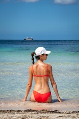 Attractive Caucasian female in a coral bikini and a cap sunbathing on the beach