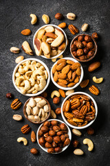Assortment of nuts in bowls. Cashew, hazelnuts, pecan, almonds, brazilian nuts and pistachios. Top view with at black stone table.