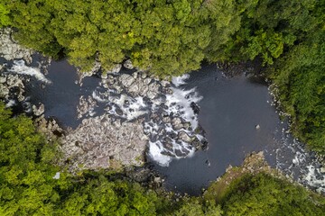 High-angle shot of a Lake in a Reunion park at the base of a waterfall that falls down a rocky crag.