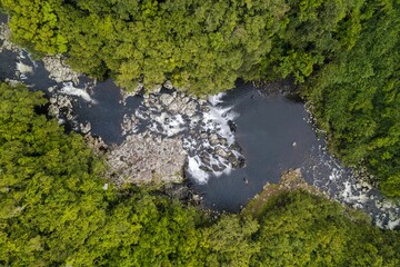 High-angle shot of a Lake in a Reunion park at the base of a waterfall that falls down a rocky crag.