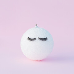 Christmas decoration bauble with eyelashes on a pink background. Holiday aesthetic beauty cosmetic concept.