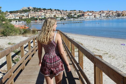 Blond woman walking on a wooden bridge with a background of the Calvi commune