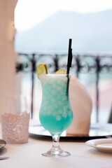 Vertical view of a blue cocktail with slices of tangerine served on a table
