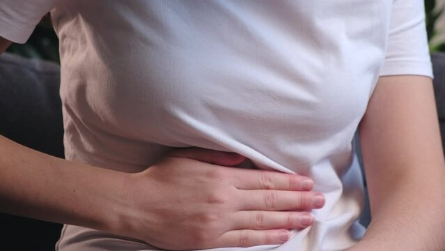 Pain in right side, appendix, gallstones and gynecological diseases concept. Close up of young woman with fatty liver touches right side with hand, suffering from abdominal pain sitting on couch