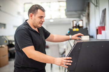 In the printing house, an experienced technician works on a UV printer. Production work. Check the print quality.