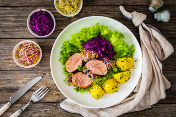 Fried pork loin with boiled potatoes and vegetables on wooden table
