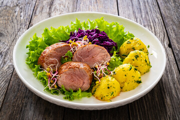 Fried pork loin with boiled potatoes and vegetables on wooden table
