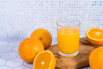 Glass of orange juice squeezed over a board and oranges around it.