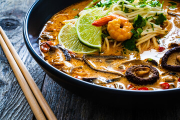 Tom Yum - Thai soup with prawn, shiitake mushrooms and noodles on wooden table
