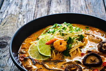 Tom Yum - Thai soup with prawn, shiitake mushrooms and noodles on wooden table
