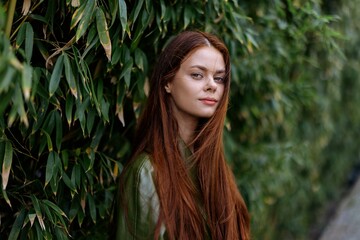 Portrait of happiness woman with red flying hair smile with teeth walking in the city in the park against a backdrop of green bamboo leaves, spring in the city