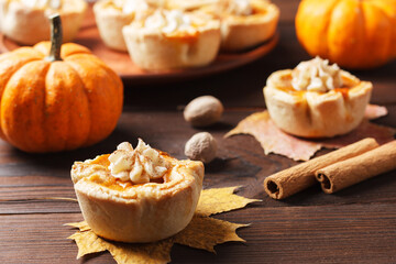 Pumpkin mini pies with whipped cream and spices on a wooden background