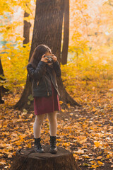 Child girl using an old-fashioned camera in autumn nature. Photographer, fall season and leisure concept.