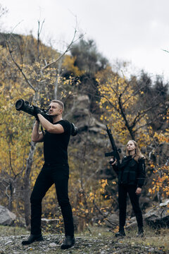 Guy and girl in military with bazooka and machine guns pose for camera