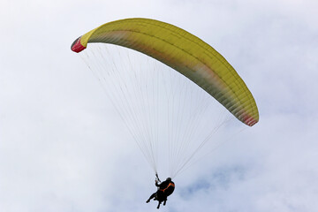 Yellow tandem Paraglider flying in a cloudy sky	