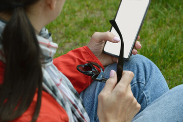A girl in blue jeans and a red jacket holds a phone glasses in her hand. Free space for text....