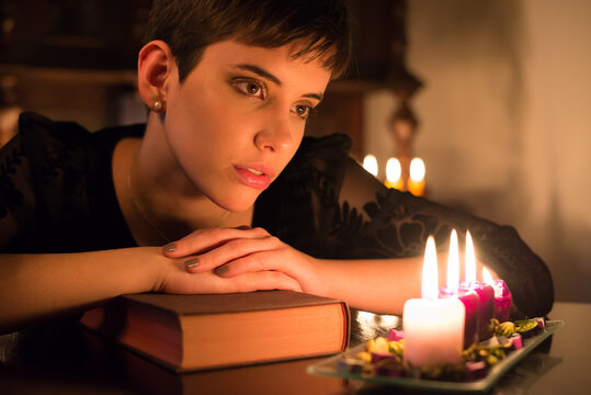 Beautiful young woman in old fashioned black dress reading book under candlelight at night - Powered by Adobe