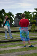 A woman tourist takes a photo of a young man in a sarong, Bali, Indonesia