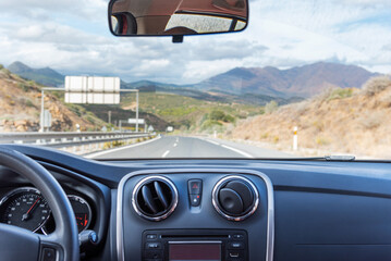View of the motorway and a landscape of mountains from inside a car driving on the road.