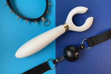 Sex shop assortment. White vibrator,  collar, gag on blue background. BDSM toys