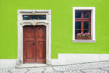 Wooden door home entrance. Window with flower box. Italian architecture background. Vibrant color yellow wall facade. Small town house exterior. Street of European city building.