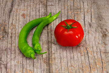 one red tomato on an old board with green peppers next to it