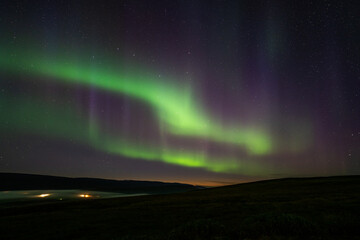 colorful northern light (Aurora) in the night sky with mountain, fog, horizon and small village