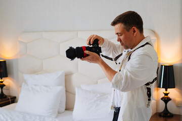 A male photographer in a white shirt with a camera takes a photo in the bedroom.