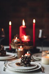 Rustic table decor for Christmas or New Year family dinner. Centrepiece with red candle, dry orange, cone, cinnamon, anise. Zero waste eco-friendly home. Cozy atmosphere, dark background. Close up