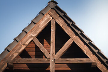 Roof truss in the setting sun. Wooden, thick beams, thick planks, brown structure supporting the roof. Roof with tiles.