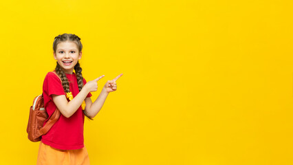 A schoolgirl points to your advertisement on a yellow isolated background. Additional training courses for schoolchildren. A happy little girl points to the ad.