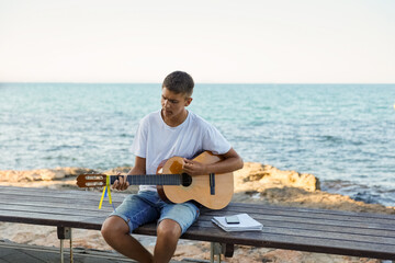 A young stylish guy plays the guitar on the embankment by the sea, the concept of music and relaxation