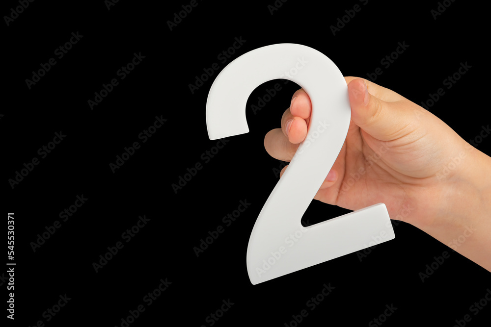 Fototapete number two in hand isolated on black background. number two white in a child's hand on a black backg