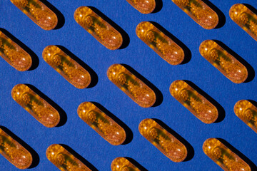 Pattern of yellow transparent liquid capsules with granules on a blue background. Medicaments aesthetically pleasing for advertising.