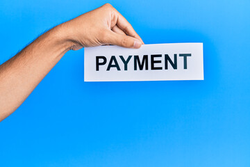 Hand of caucasian man holding paper with payment word over isolated blue background