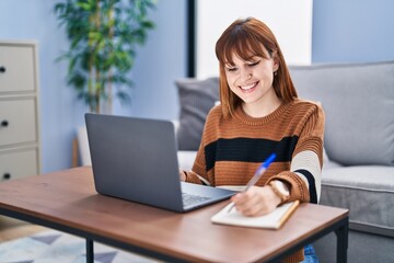 Young woman using laptop writing on notebook at home