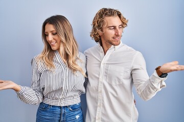 Young couple standing over blue background smiling showing both hands open palms, presenting and advertising comparison and balance