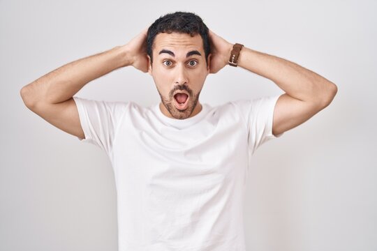 Handsome hispanic man standing over white background crazy and scared with hands on head, afraid and surprised of shock with open mouth