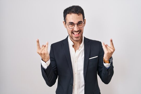 Handsome business hispanic man standing over white background shouting with crazy expression doing rock symbol with hands up. music star. heavy music concept.