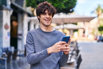 Young hispanic man smiling confident using smartphone at street