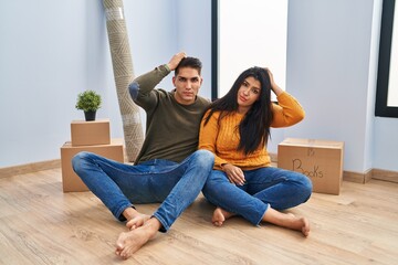 Young couple sitting on the floor at new home confuse and wondering about question. uncertain with...