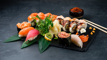 Large sushi set on slate on a black background assortment of various maki, nigiri and rolls