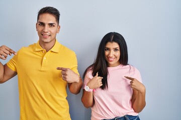 Young couple standing over isolated background looking confident with smile on face, pointing oneself with fingers proud and happy.