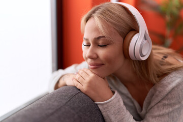 Fototapeta premium Young blonde woman listening to music sitting on sofa at home