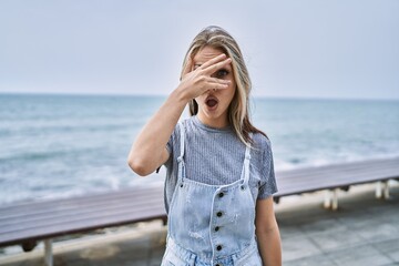 Young caucasian woman outdoors peeking in shock covering face and eyes with hand, looking through fingers with embarrassed expression.