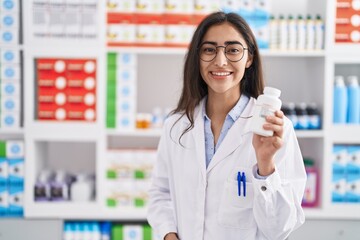 Young hispanic girl pharmacist holding pills at pharmacy
